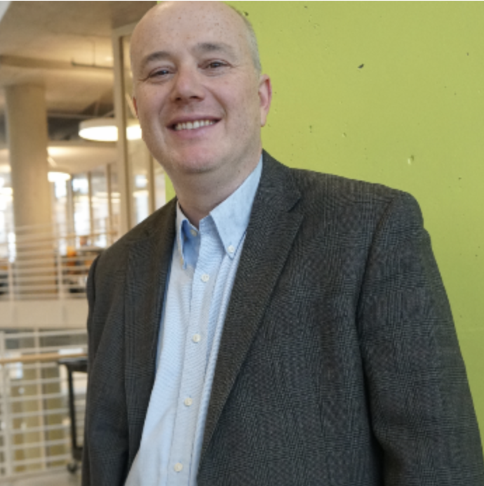 Adjunct Professor, Mikhail Pevzner. Wearing a grey suit jacket with a light blue dress shirt.